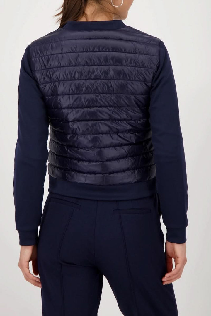 Femme portant une veste matelassée bimatière à fermeture éclair vue de dos, montrant le corps matelassé et les manches souples noires.