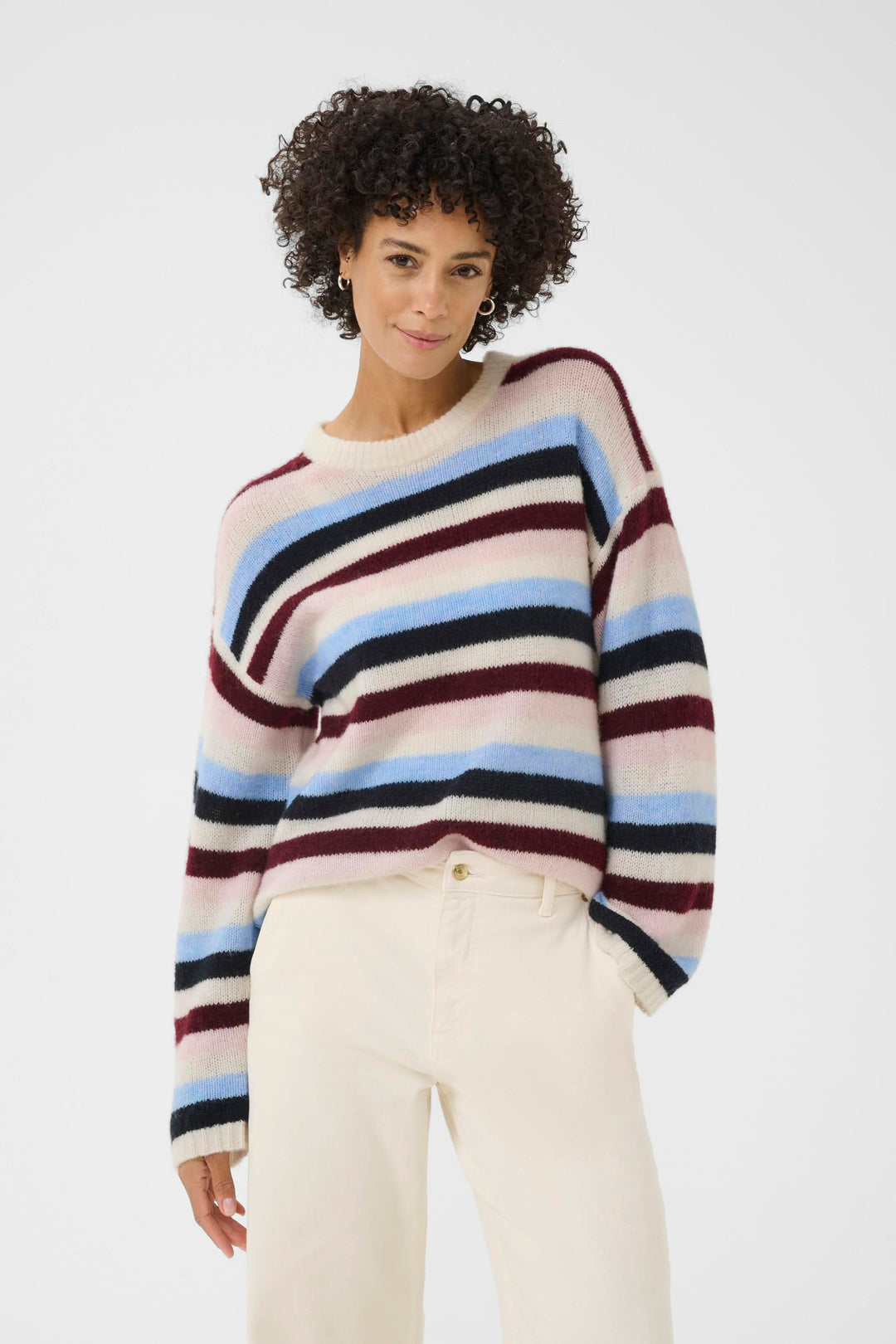 Femme portant un Tricot Spence à rayures multicolores, col rond, manches longues, style décontracté chic sur pantalon clair.