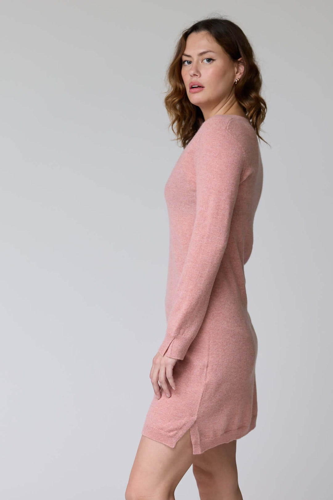 Femme portant la Robe Bonnie en tricot à col en V rose, silhouette féminine, manches longues, coupe droite élégante.