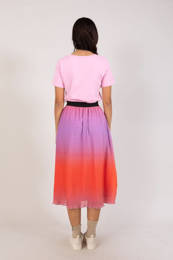 Jupe plissée dégradée en violet et rouge, portée avec un t-shirt rose et une ceinture noire.