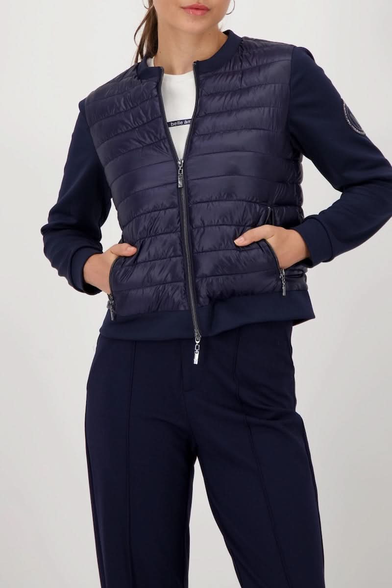 Femme portant une veste matelassée bimatière à fermeture éclair en bleu, manches souples, idéale pour un look chic et confortable.