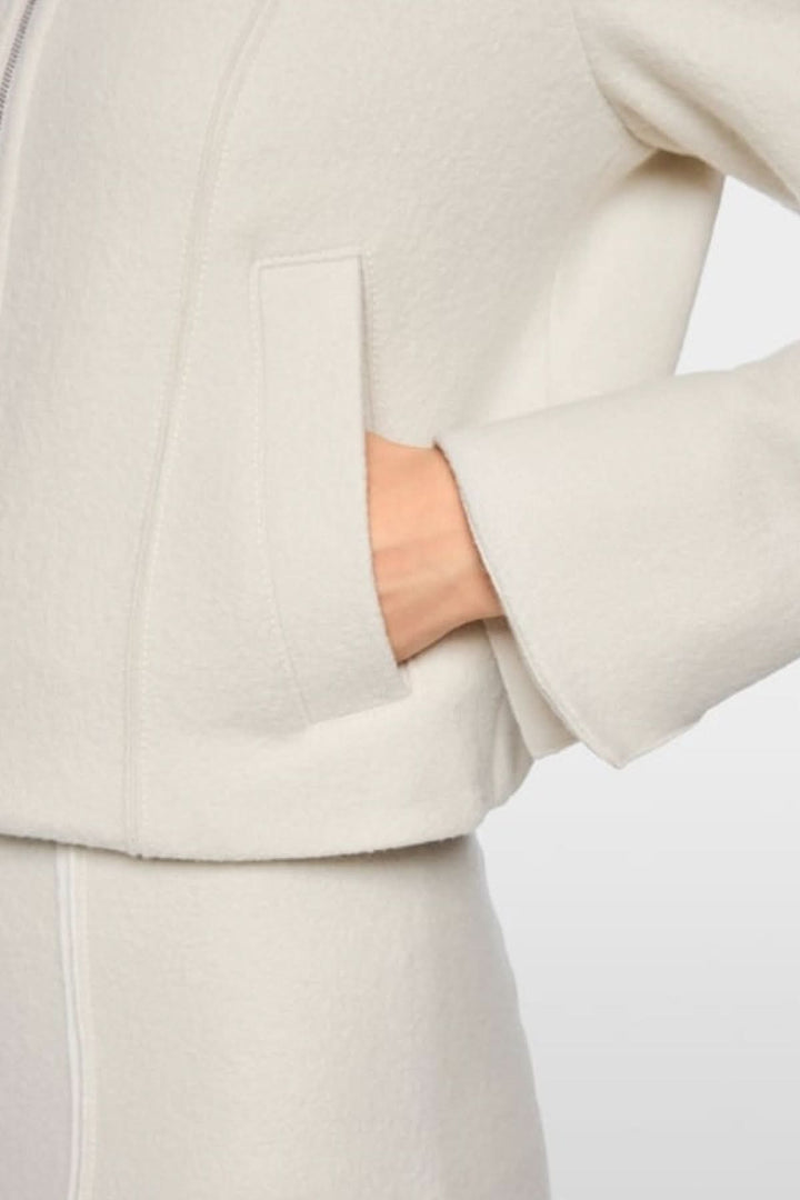 Gros plan d'une veste en laine vierge blanche avec poche passepoilée et poignets fendus, style moderne et confortable.