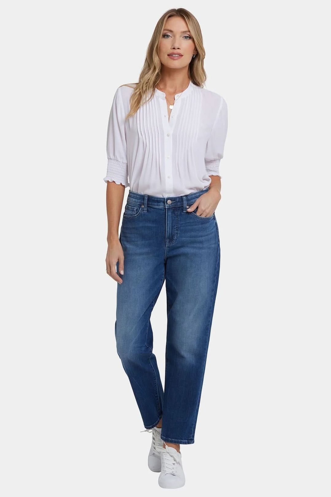 Jean boyfriend taille classique décontracté, coupe droite moderne, teinte délavée, porté avec chemise blanche et baskets.