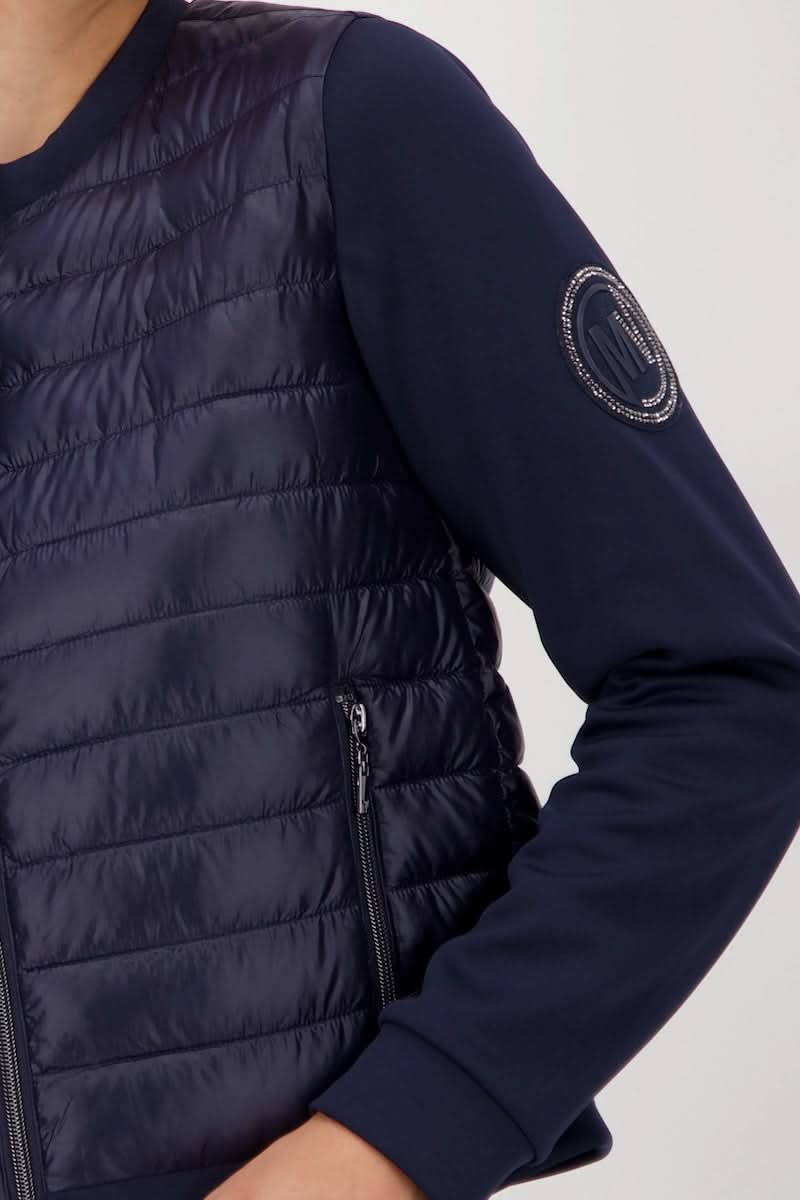 Veste matelassée bimatière à fermeture éclair avec manches souples et poche zippée, idéale pour look chic et sportif.