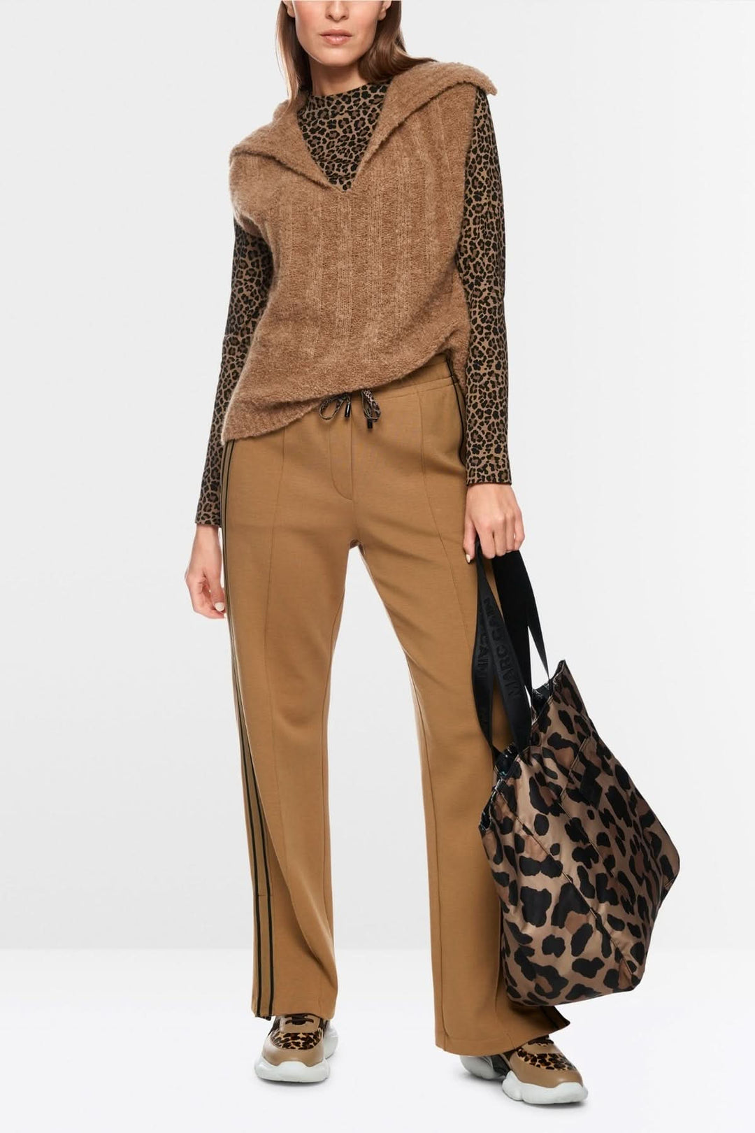 Femme portant une veste sans manche tricoté avec col en V sur une chemise à motifs, tenue moderne et élégante avec pantalon et sac animalier.