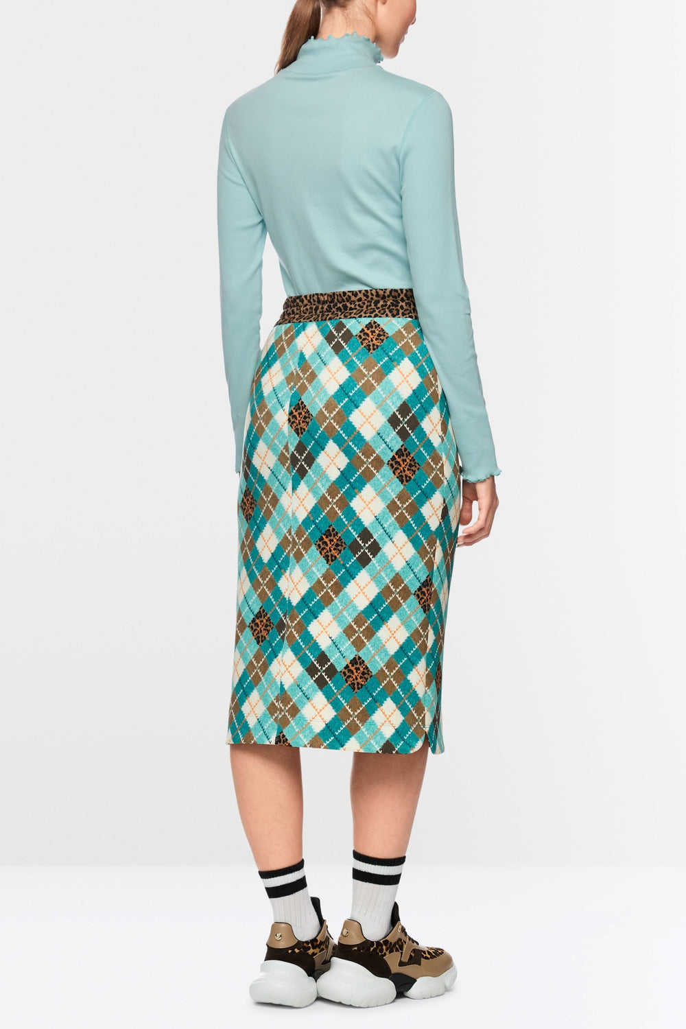 Femme portant un chandail à col montant et bordures ondulées, de dos, combiné avec une jupe à motif quadrillé multicolore.