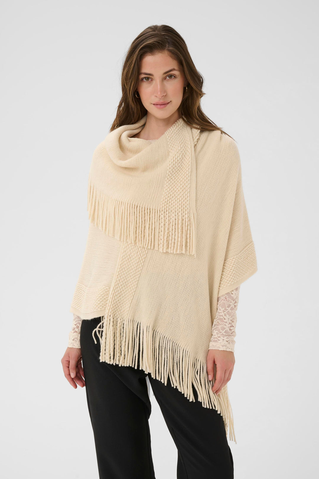 Femme portant une cape en tricot à franges beige, élégante avec un col drapé, idéale pour un style automnal et décontracté.