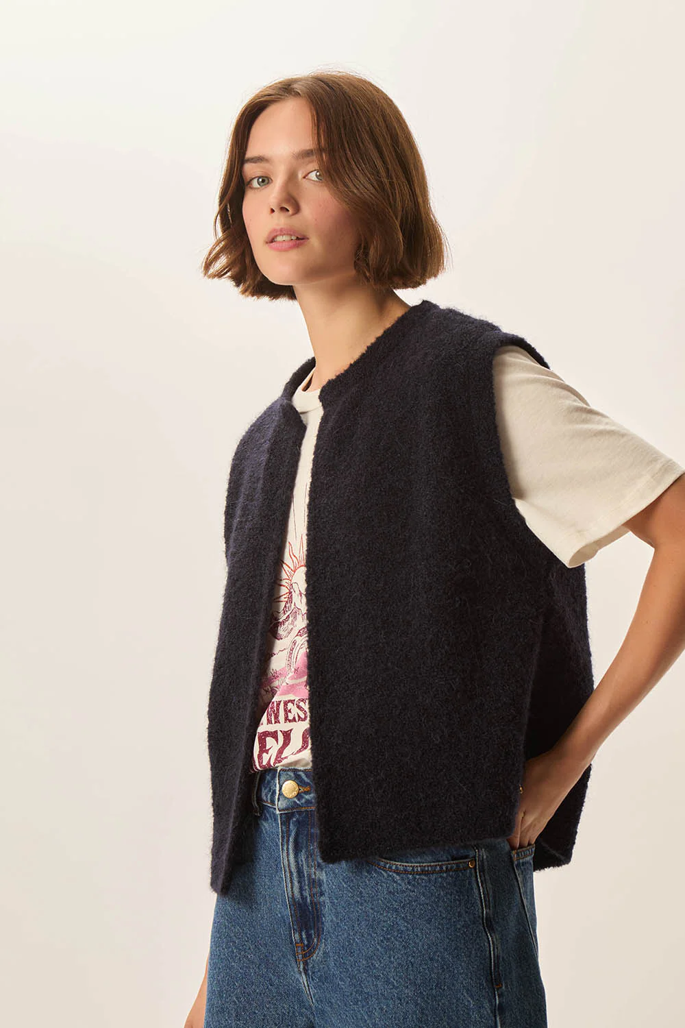 Femme portant la Veste Achille sans manches en laine bouclée noire, associée à un t-shirt imprimé et jean, style décontracté.