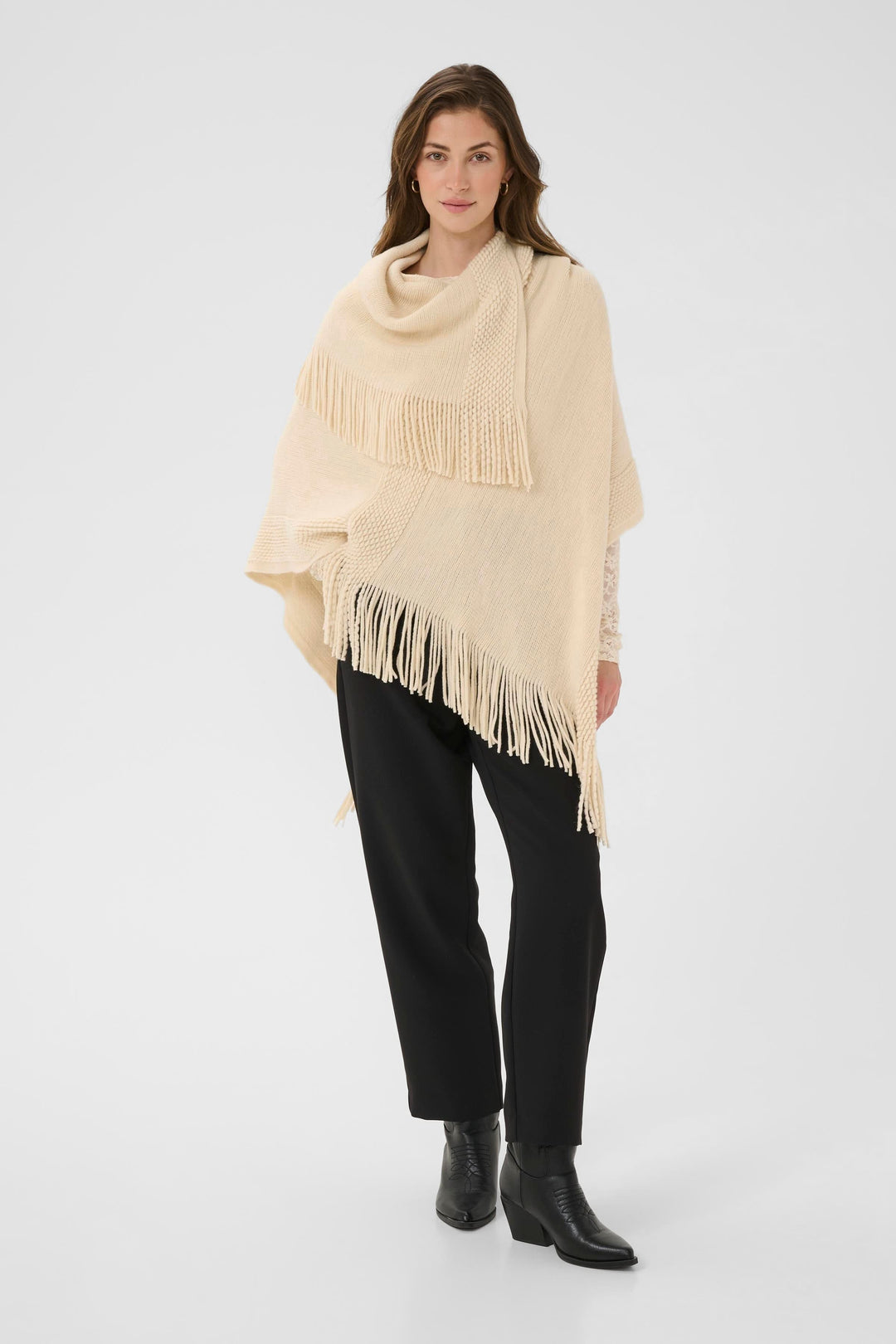 Cape en tricot à franges, élégante et décontractée, portée avec un pantalon noir et bottines. Style automnal doux et raffiné.