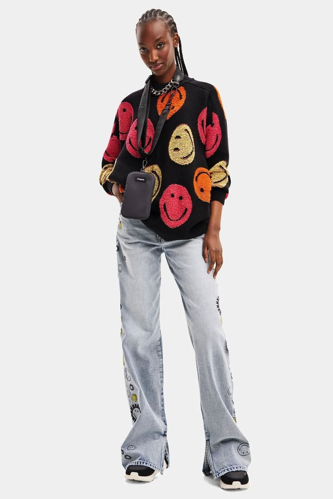 Pull ample en grosse maille jacquard noir avec imprimés de bonhommes sourire, porté avec un jean clair.