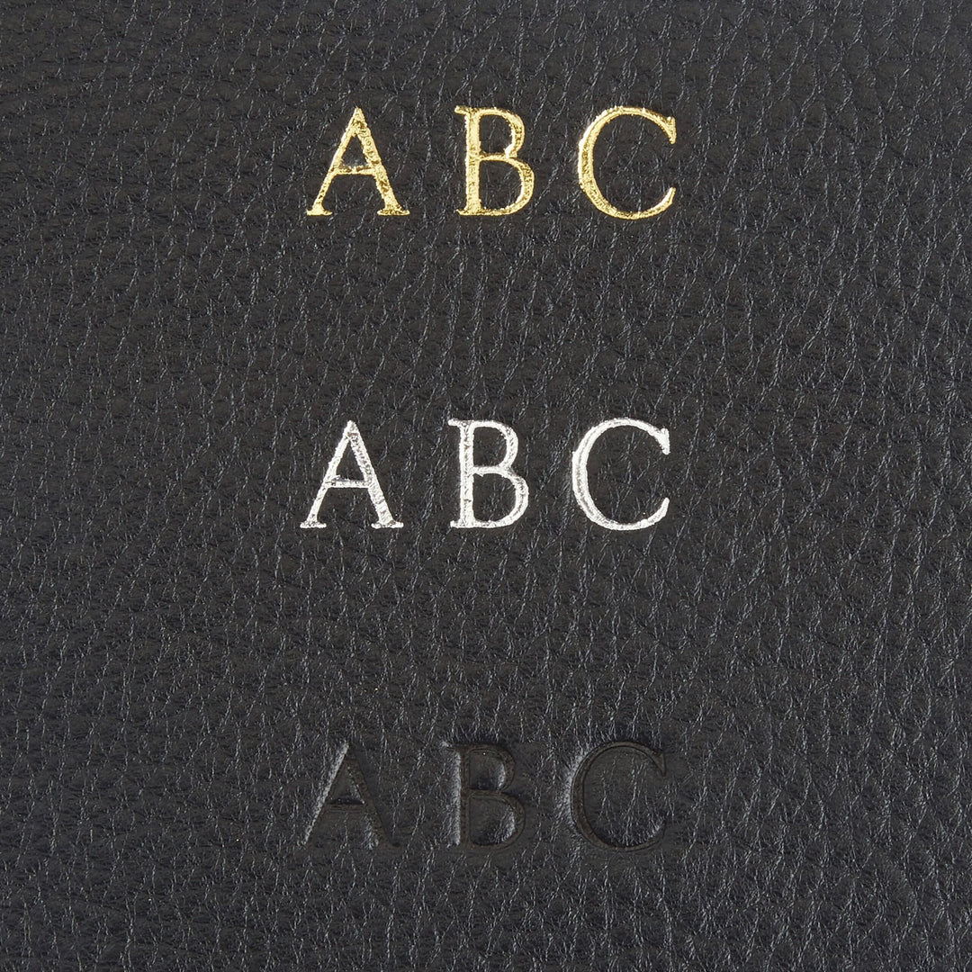 Close-up of monogrammed letters in gold, silver, and embossed on black leather for personalized door knob hanger.