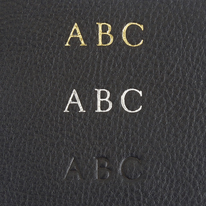 Close-up of monogrammed letters in gold, silver, and embossed on black leather for personalized door knob hanger.