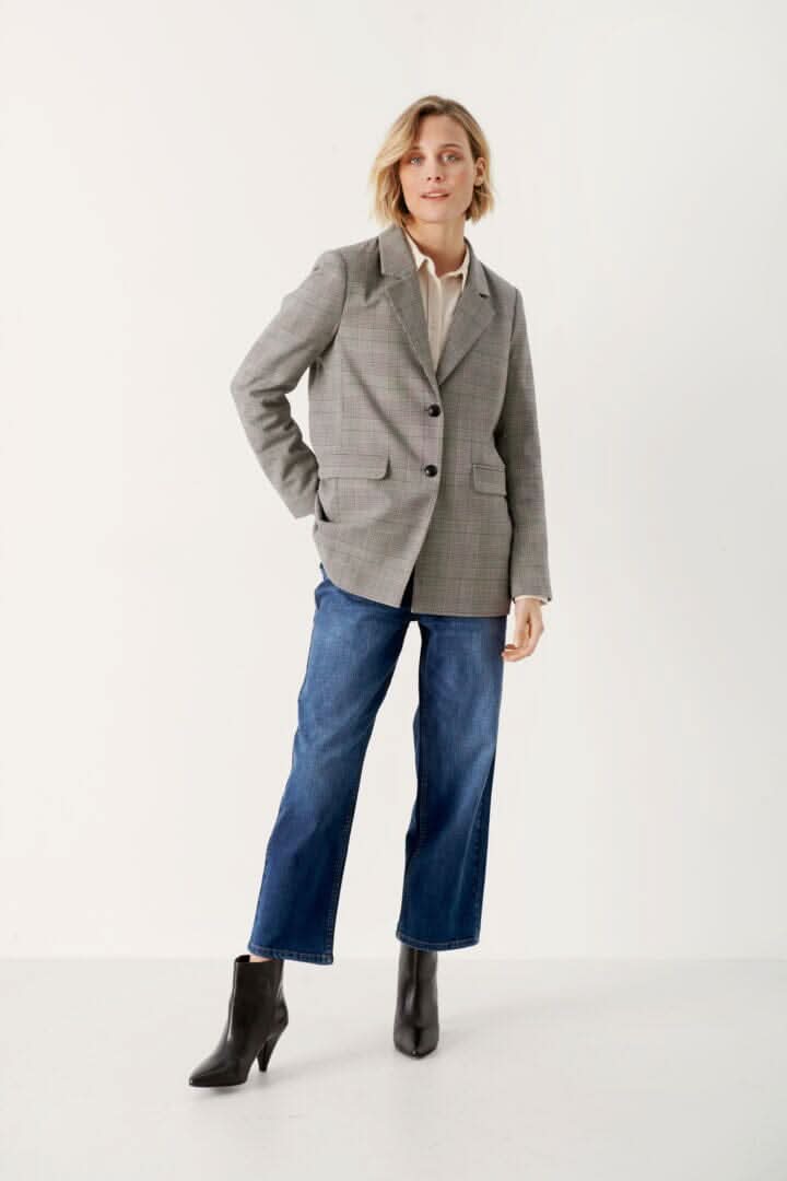 Femme en blazer à carreaux gris, jean décontracté, et bottines noires, style moderne et élégant.